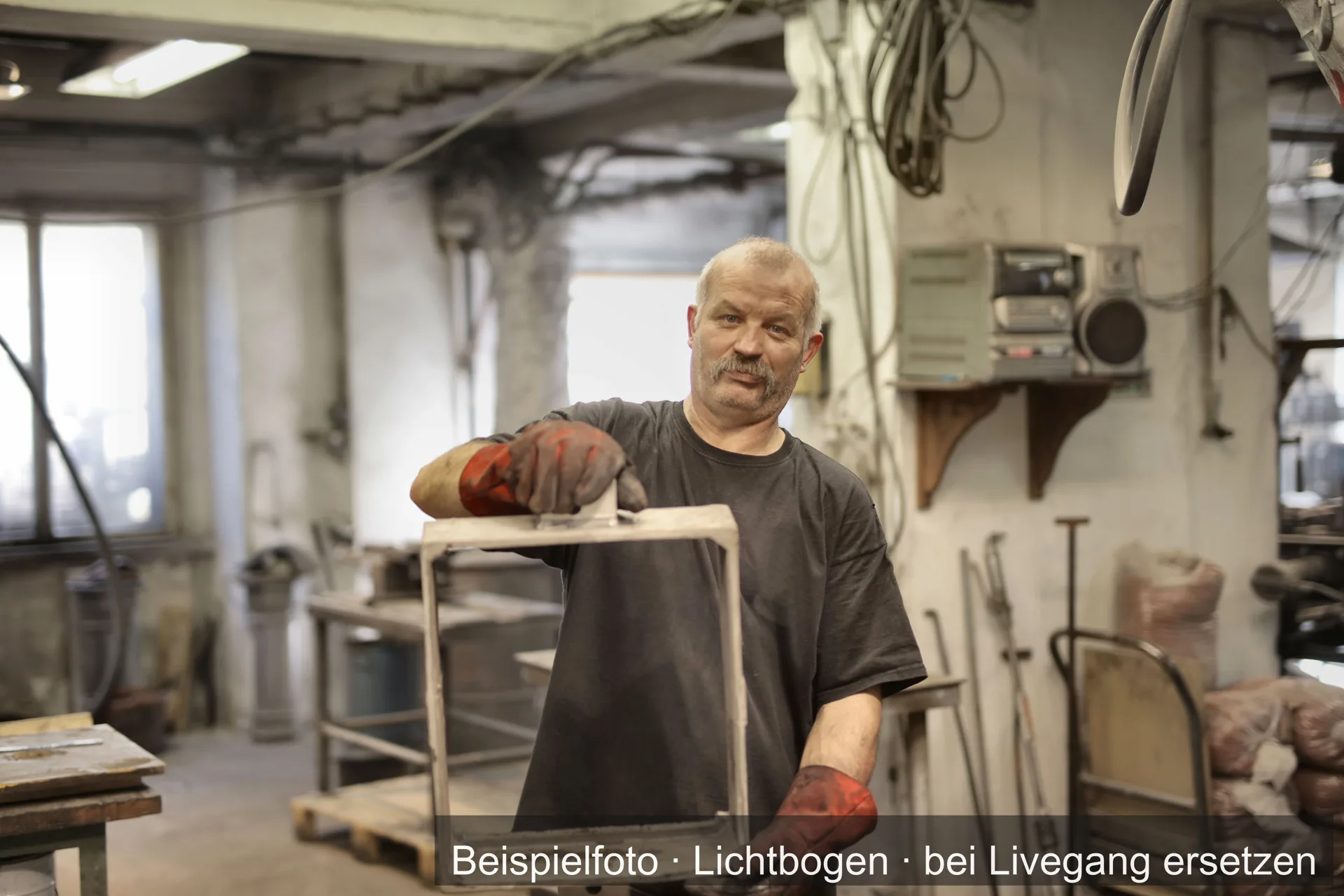 Metallhandwerker mit Arbeitshandschuhen hält ein Werkstück in einer Werkstatt.