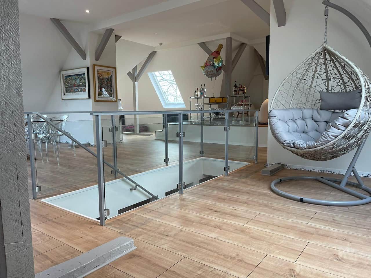 Glasgeländer mit runden Edelstahlpfosten um eine Treppenöffnung in einem ausgebauten Dachgeschoss.