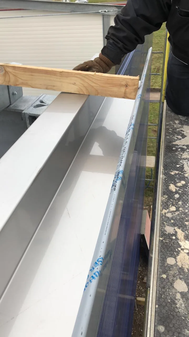 Ein weißes Kantteil mit Schutzfolie wird mit Arbeitshandschuh an einer Brüstung angehalten.