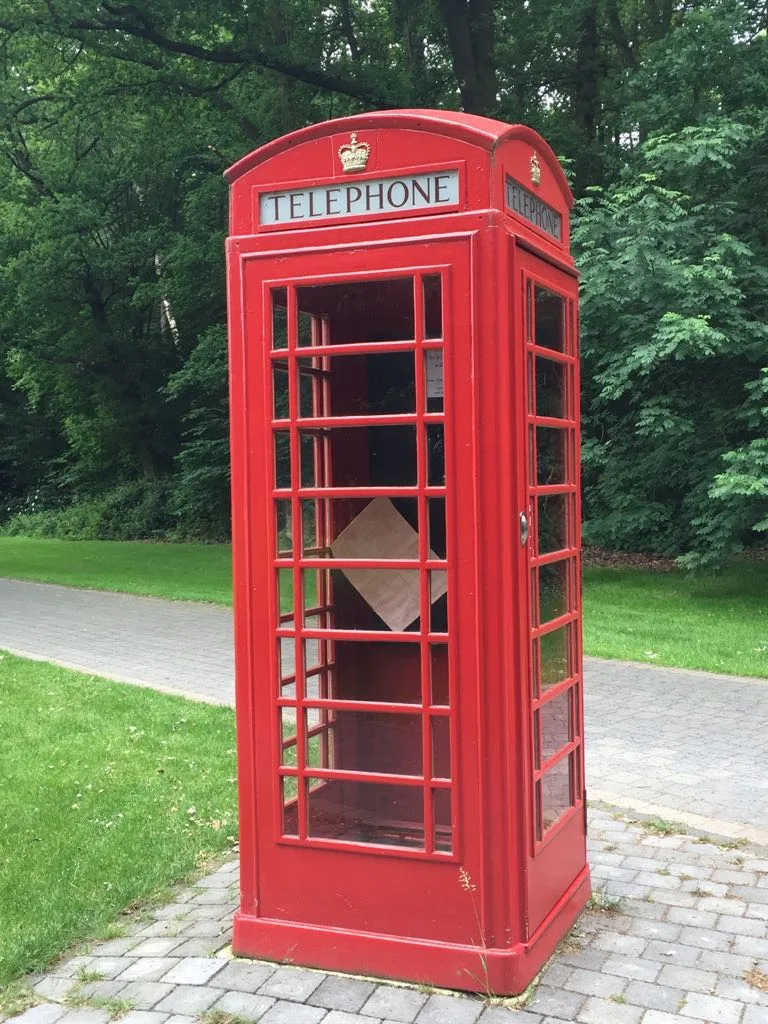 Restaurierte rote britische Telefonzelle, aufgestellt an einem Weg.